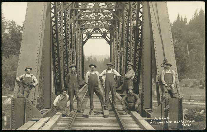 Old black and white photograph of railroad workers standing on a railroad bridge.
